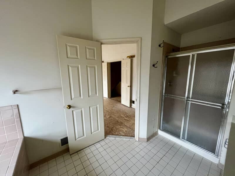 Primary bathroom with glass-enclosed shower, tile flooring, and white door leading to hallway.