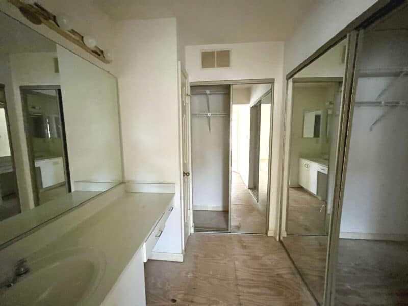 Primary suite vanity area with large countertop, wall mirror, and mirrored closet doors.