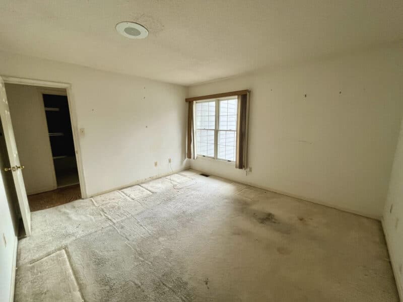 Spacious second-floor bedroom with light carpet, large front-facing window, and neutral walls.