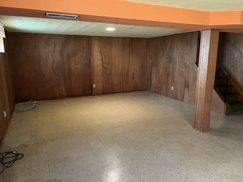 Alternate view of basement recreation room showing paneling, support beam, and open layout.
