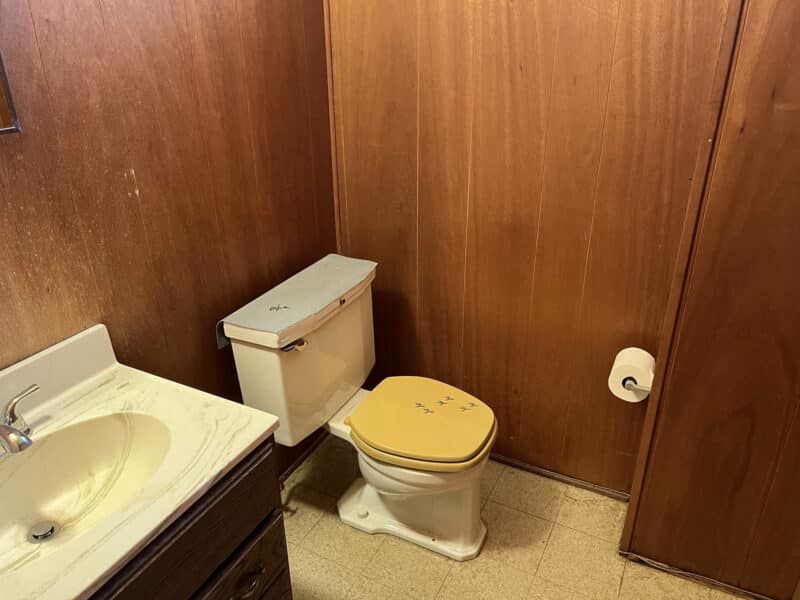 Lower-level half bath with wood paneling, vanity, and yellow toilet seat at 4729 Byron Road.
