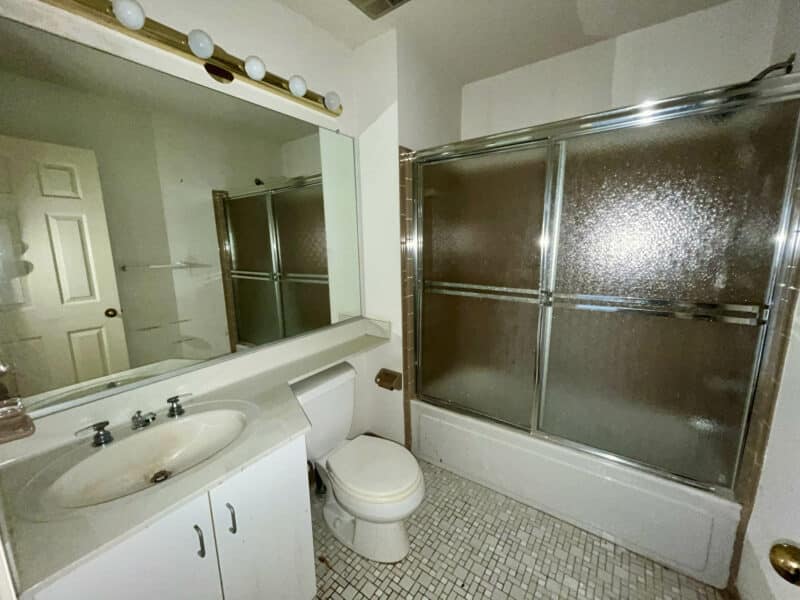 Hall bathroom with tile floor, single vanity, and tub/shower combination with sliding glass doors.