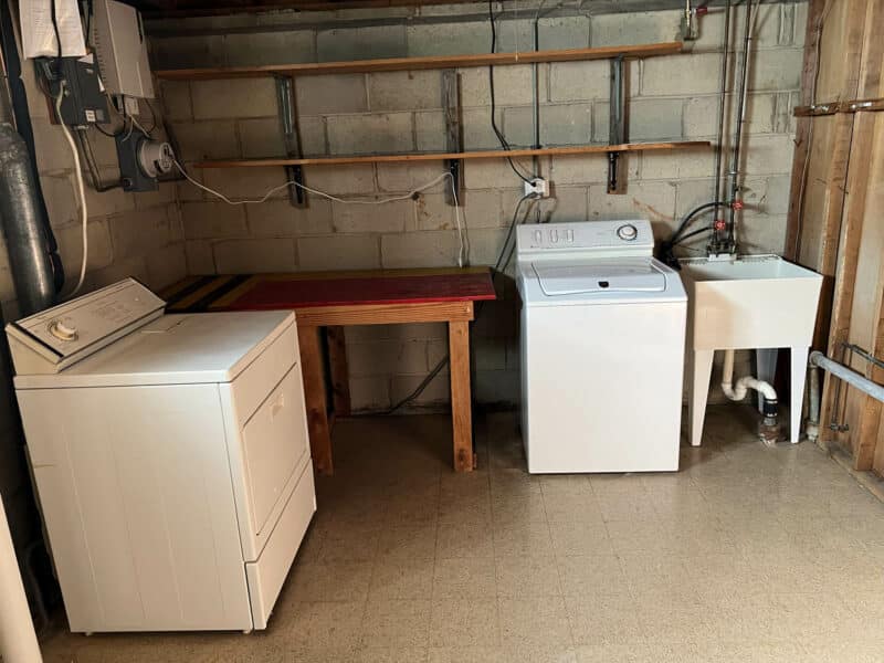 Laundry area in the basement featuring washer, dryer, utility sink, shelving, and exposed block walls at 4729 Byron Road, Pikesville.
