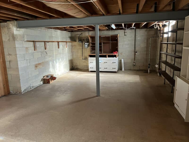 Large unfinished basement with open layout, exposed ceiling beams, shelving, and storage space at 4729 Byron Road, Pikesville.