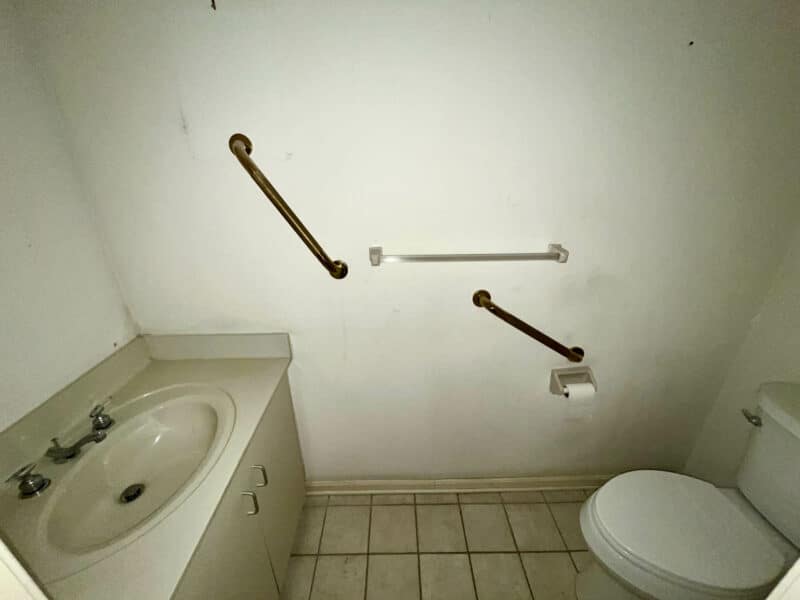 Bathroom with single vanity, toilet, tile flooring, and multiple safety grab bars installed.