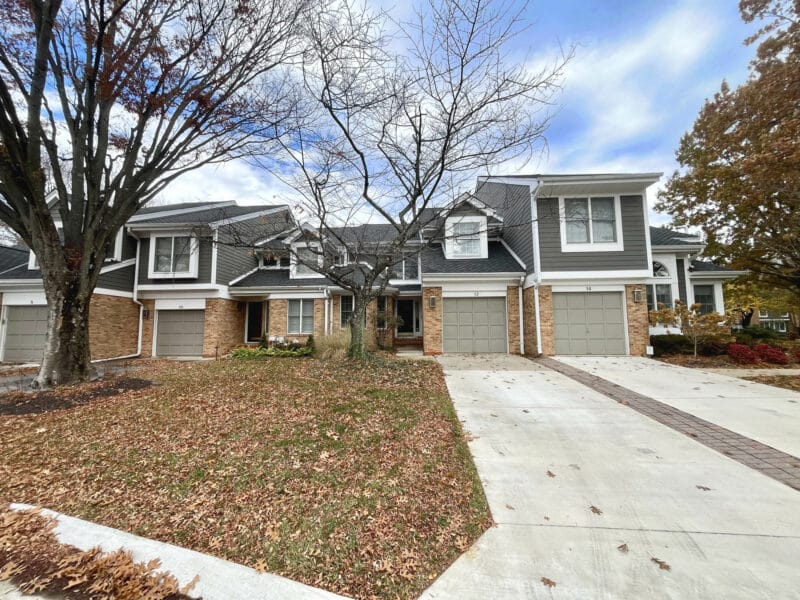 Front exterior of a two-story townhome in the Greene Tree community with brick and siding façade, driveway, and mature landscaping.