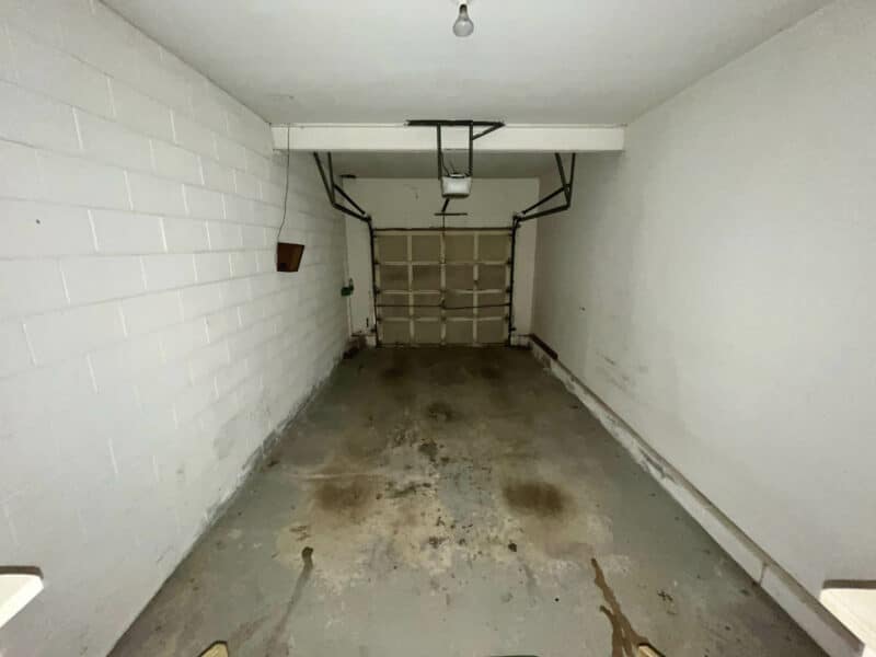 Deep one-car garage with concrete floor, overhead door, and ceiling-mounted opener.