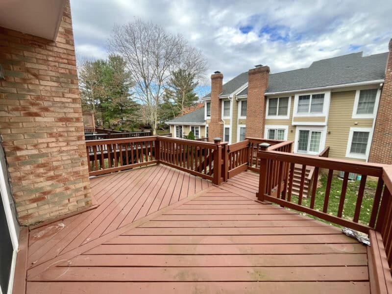 Large wooden deck with railings overlooking neighboring homes and landscaped common space.
