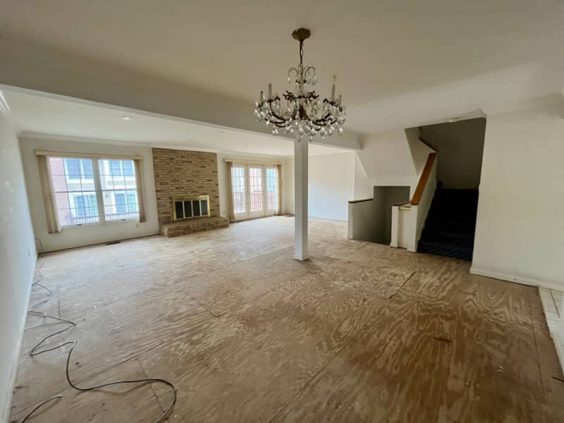 Large living room with exposed subfloor, brick fireplace, chandelier, and sliding doors leading to the deck.