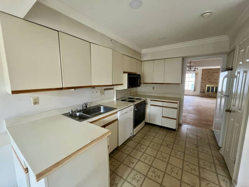 Spacious kitchen with white cabinetry, wraparound counters, tile flooring, and large windows providing natural light.