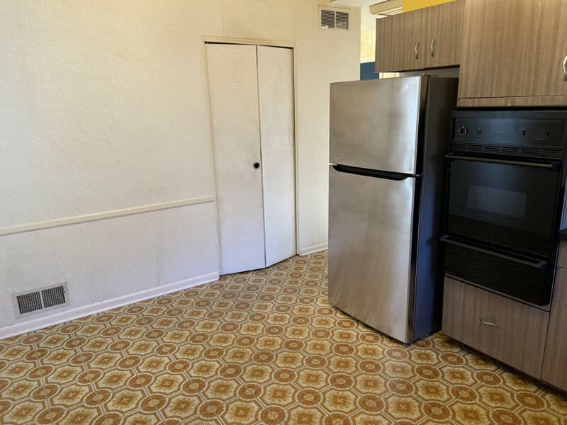 Eat-in kitchen area with patterned vinyl flooring, white walls, refrigerator, and built-in wall oven.