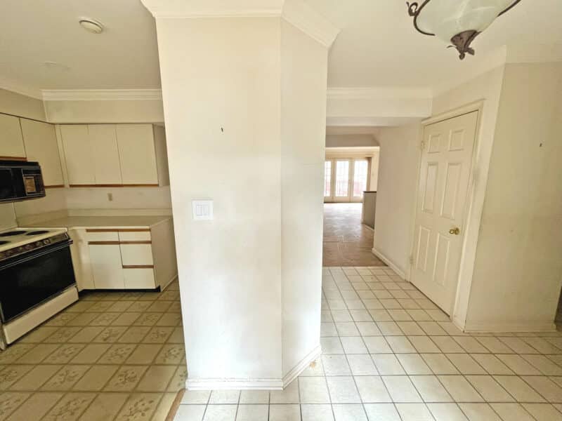 View from kitchen into rear hallway with white cabinetry, tile flooring, and multiple doorways.