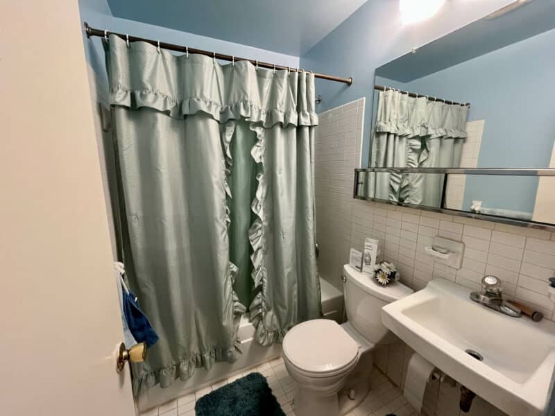 Full bathroom with tile floor, tub/shower combo, green ruffled shower curtain, and pedestal sink.