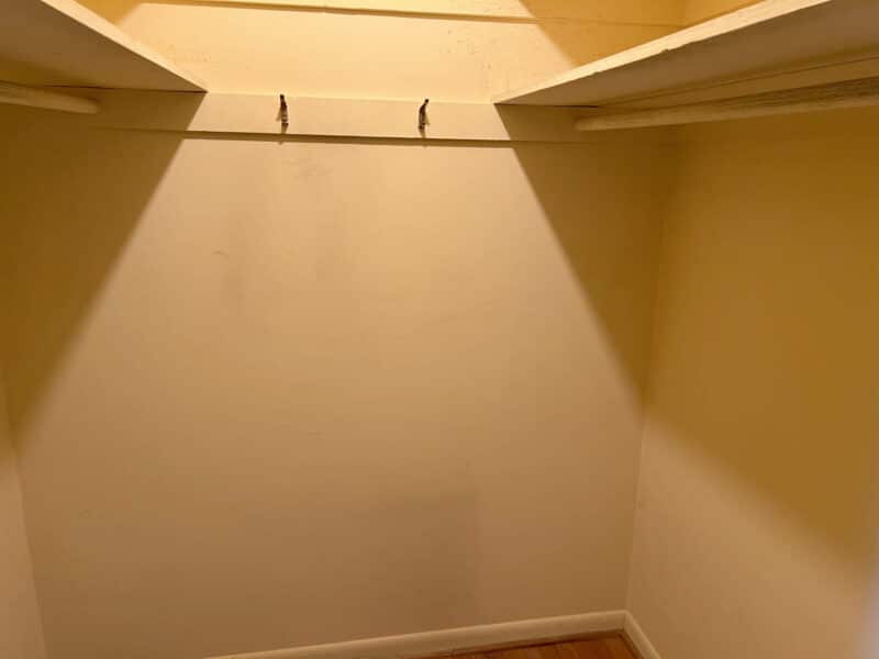 Empty walk-in closet or small storage room with built-in upper shelving and yellow painted walls.