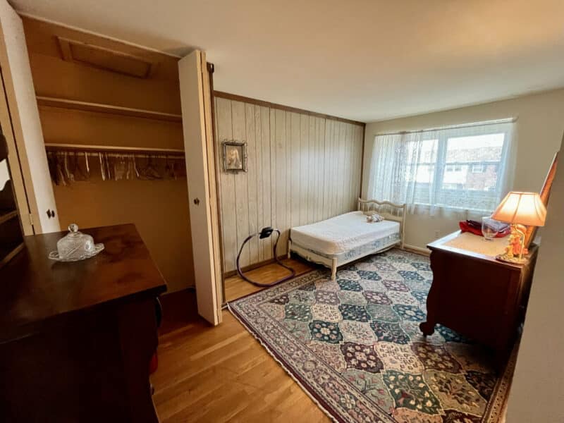 Bedroom with wood-paneled accent wall, hardwood flooring, and window overlooking the yard.