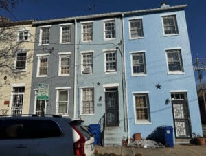Front exterior view of the three-story brick townhome at 703 Tessier Street in Seton Hill, Baltimore, featuring pastel-painted facades, traditional window styles, and a walk-up entry.