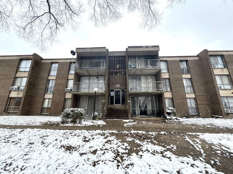 Alternate front exterior view of The Marylander condominium with balconies, brick façade, and snow on the ground.
