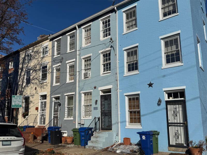Another exterior shot of 703 Tessier Street and adjacent rowhomes, showing pastel facades, walk-up stoops, and street parking.