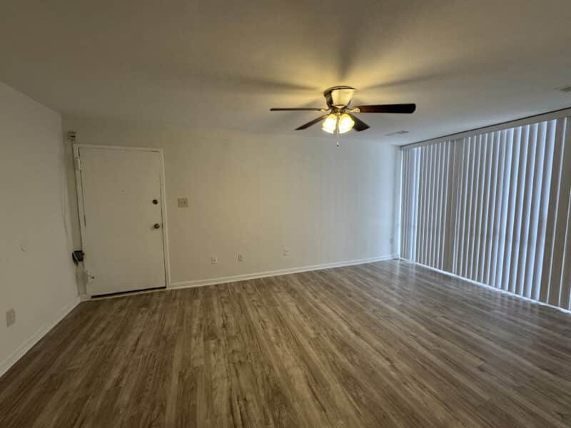 Renovated living room with new vinyl plank flooring, ceiling fan, and sliding glass doors leading to a private balcony at 7969 Riggs Road, Unit 7.
