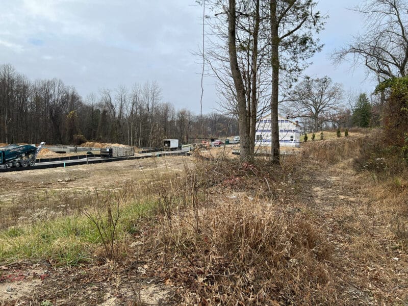 Open field on the Stokers Lane parcel with trees on the right and active residential development and construction materials visible in the distance.