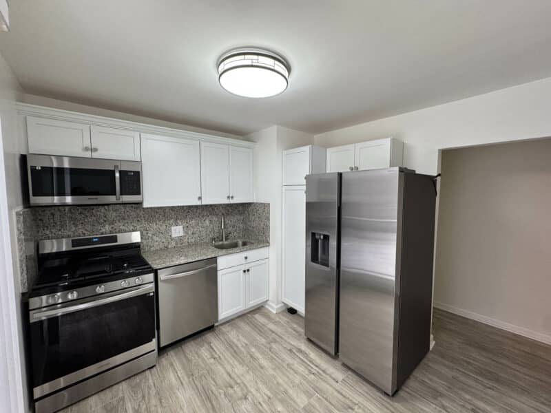Renovated kitchen with white cabinetry, stone countertops, stainless steel appliances, and wood-style flooring.