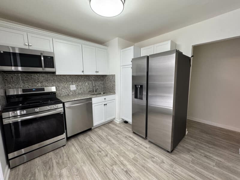Updated kitchen with stainless steel refrigerator, gas range, built-in microwave, and white shaker cabinets.