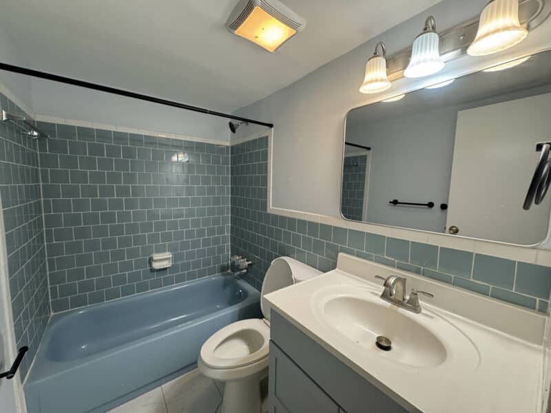 Bathroom with blue tile surround, soaking tub, updated vanity, modern lighting, and ceramic tile flooring.