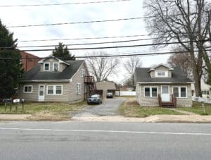 Front view of multi-building property at 8224–8226 Fort Smallwood Road featuring two bungalows, gravel driveway, and rear barn structure in Pasadena, MD