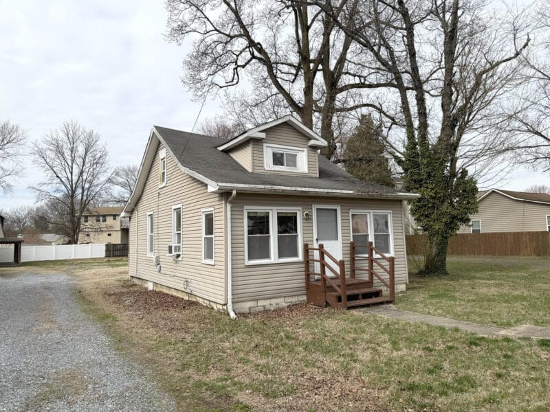 Exterior of vinyl-sided bungalow at 8224 Fort Smallwood Road with small front porch and gravel driveway access