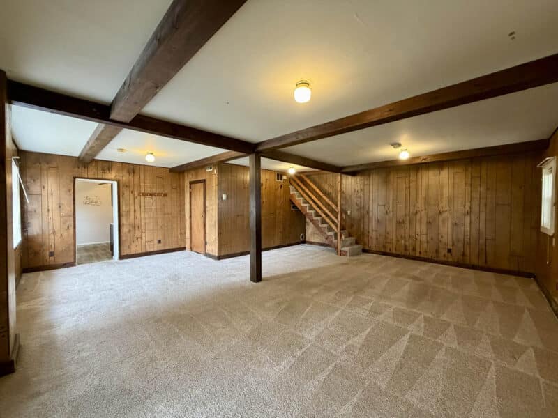 Open living area with exposed beams, wood-paneled walls, and carpet flooring in converted barn at 8226 Fort Smallwood