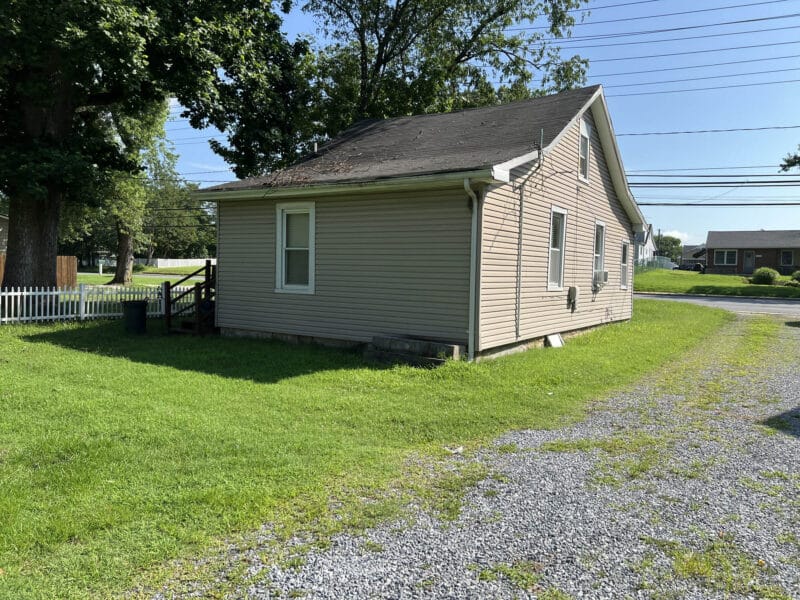 Side exterior view of 8224 Fort Smallwood Road bungalow with vinyl siding, gravel driveway, and fenced yard area