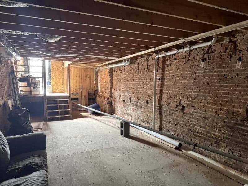 Basement area with stair access, exposed brick, and unfinished interior ready for redevelopment