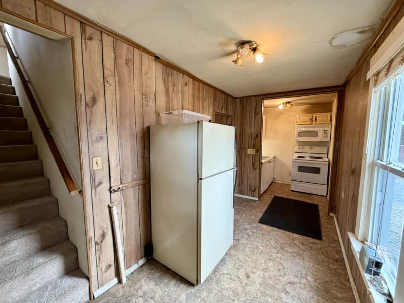 Interior view showing staircase, refrigerator, and entry to kitchen area with wood-paneled walls
