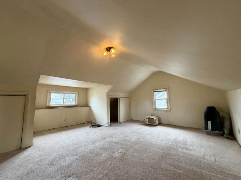 Upper-level bedroom with sloped ceilings, carpet flooring, and window AC unit