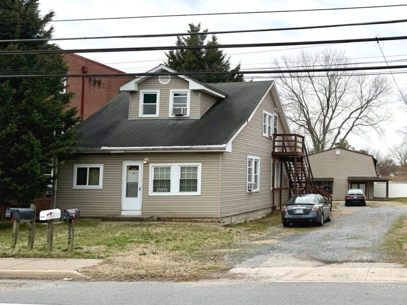 Front exterior of apartment building at 8226 Fort Smallwood Road with gravel driveway, exterior staircase, and parking area