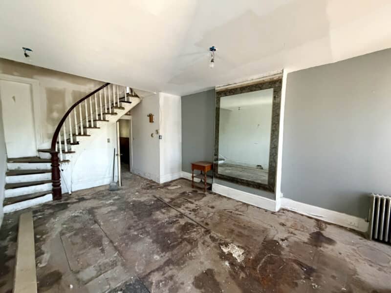 Living room interior with original staircase and unfinished flooring in Harlem Park shell townhome.