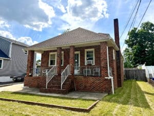 Front exterior of all-brick porchfront bungalow with covered porch and architectural shingle roof in Essex, Maryland.