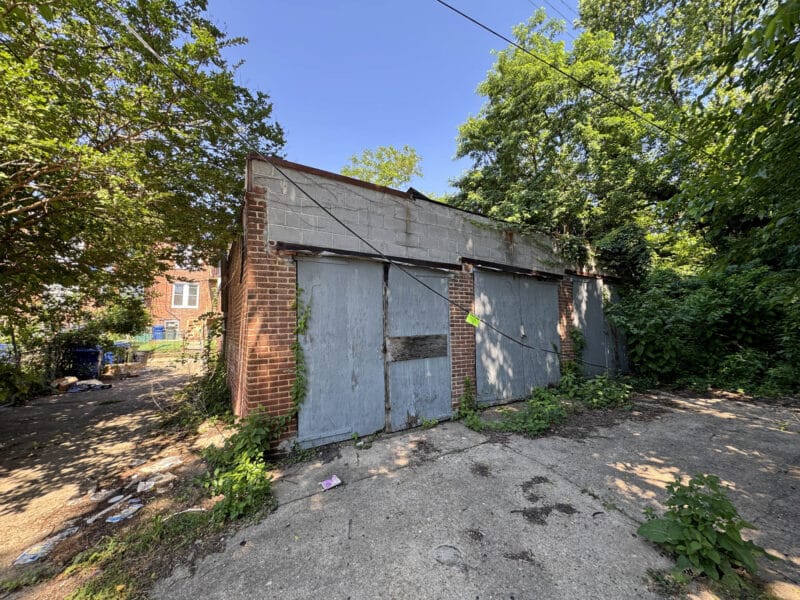 Front exterior view of six-garage-space masonry building with multiple metal garage doors and alley access in West Baltimore.