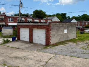 Two-bay concrete masonry garage building with white overhead doors and adjoining paved parking area in Baltimore's Belair-Edison neighborhood.