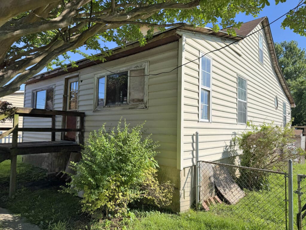 Side exterior view of 1124 North Point Road, a vinyl-sided bungalow in Dundalk, Maryland with fenced yard and mature landscaping