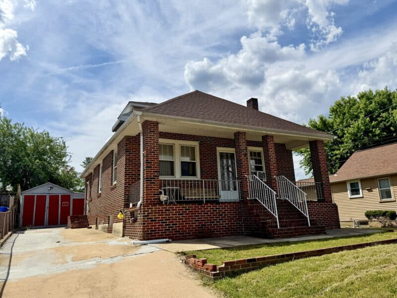 Front exterior of brick bungalow with concrete driveway leading to detached garage.