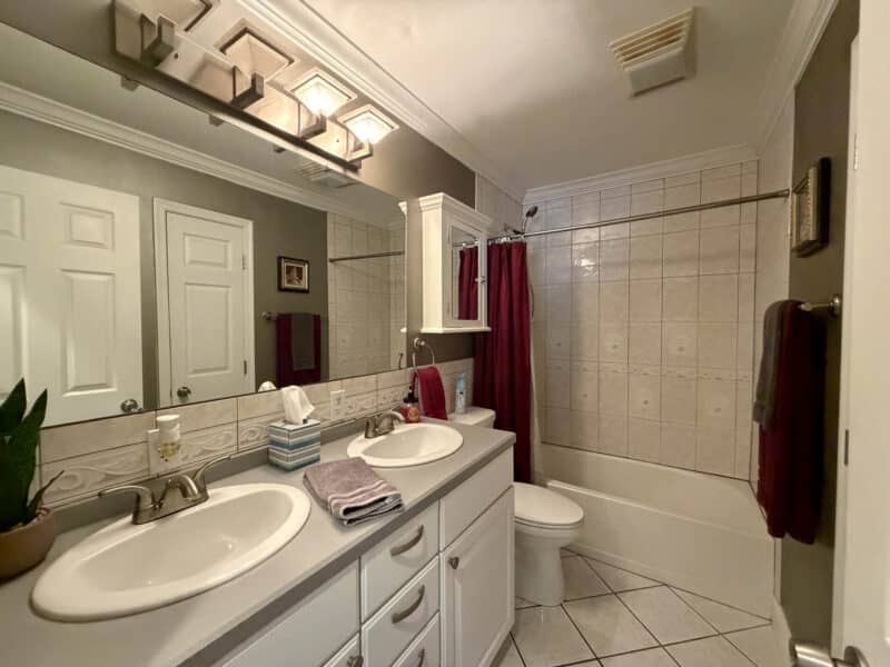 Full bathroom with double vanity, tiled tub and shower surround and tile flooring.