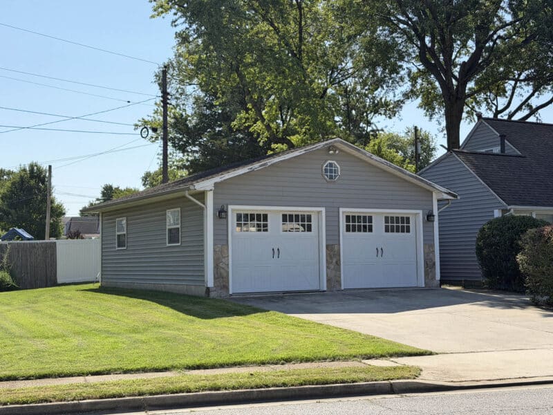 Detached two-car garage with two overhead doors, siding and stone accents.