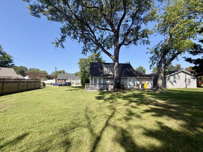 Rear exterior of Cape Cod home overlooking spacious backyard with mature trees and lawn.