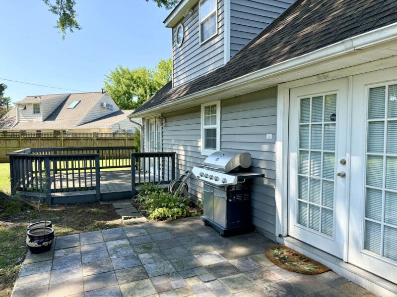 Rear deck and patio with grill providing outdoor entertaining space behind Cape Cod home.