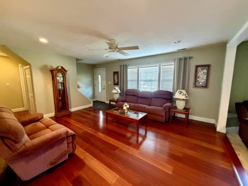 Living room with hardwood flooring, ceiling fan, recessed lighting and large front windows.