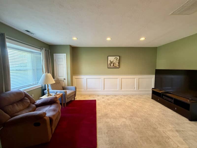 Carpeted family room with recessed lighting, large window and decorative wall panel molding.