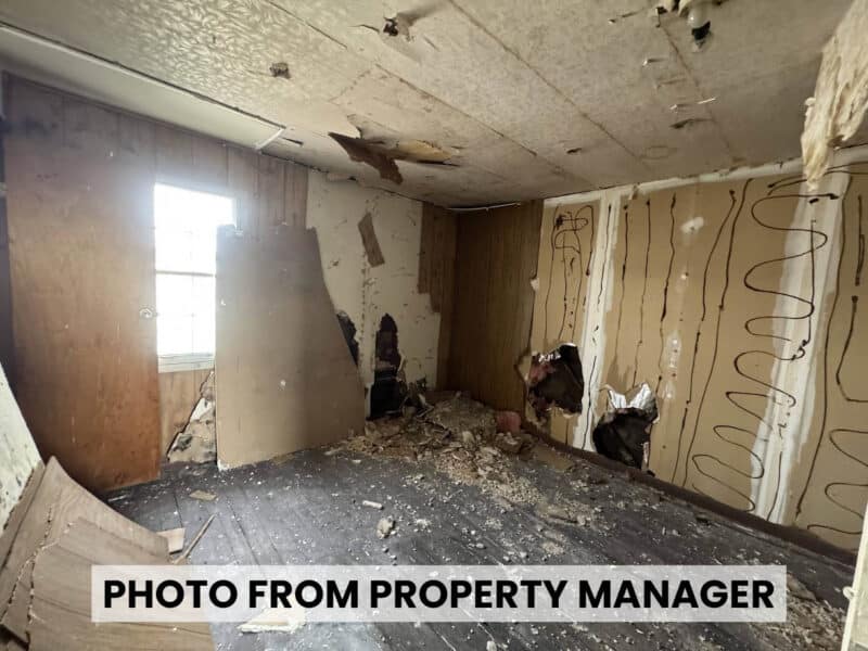Damaged residential interior at 4900 Curtis Avenue showing deteriorated ceiling, holes in walls, exposed flooring, and construction debris.
