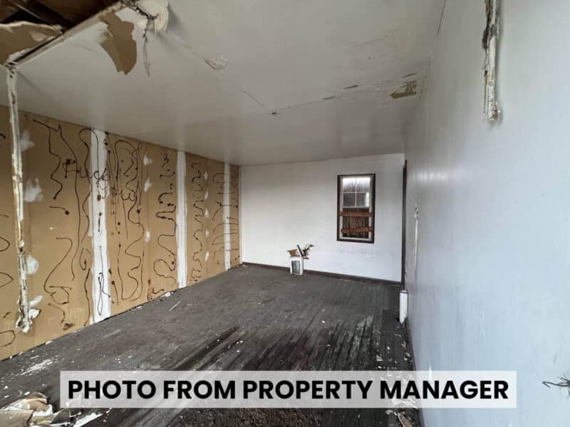 Vacant room at 4900 Curtis Avenue in Baltimore showing exposed wood floors, unfinished wall surfaces, and damaged ceiling plaster.