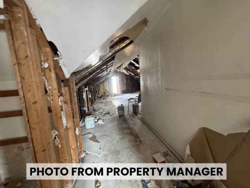 Unfinished upper-level interior at 4900 Curtis Avenue showing sloped ceiling, exposed wall framing, wood flooring, and renovation debris.